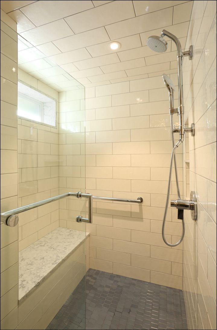 Accessible shower with bench, grab bars, and handheld showerhead, tiled walls.