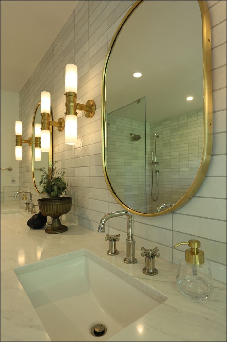 Bathroom with white sink, gold mirror, sconces, and light-colored tile.