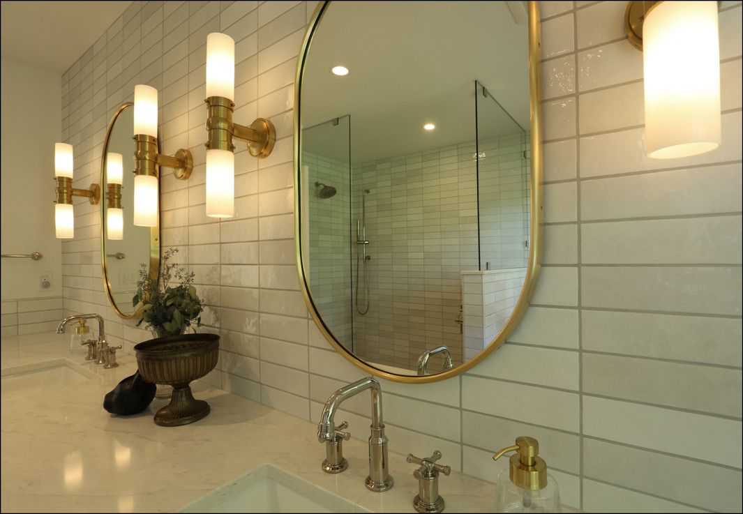 Bathroom with oval mirrors, gold fixtures, and white tile walls.