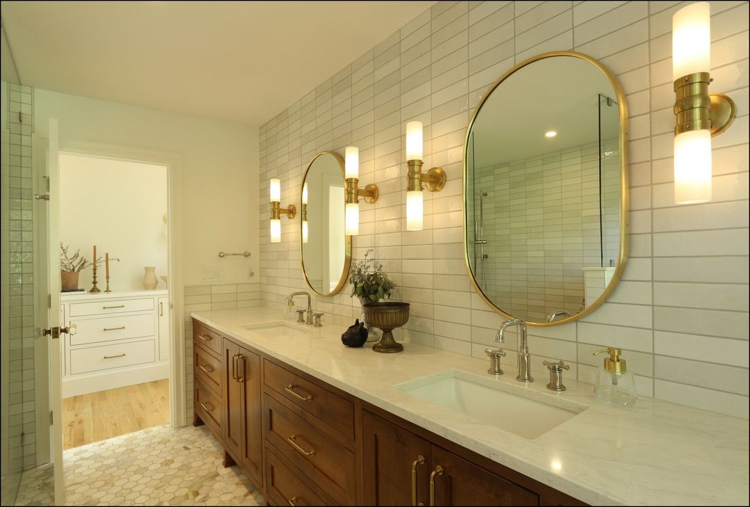 Bathroom with oval mirrors, sconces, wood vanity, and white tile.