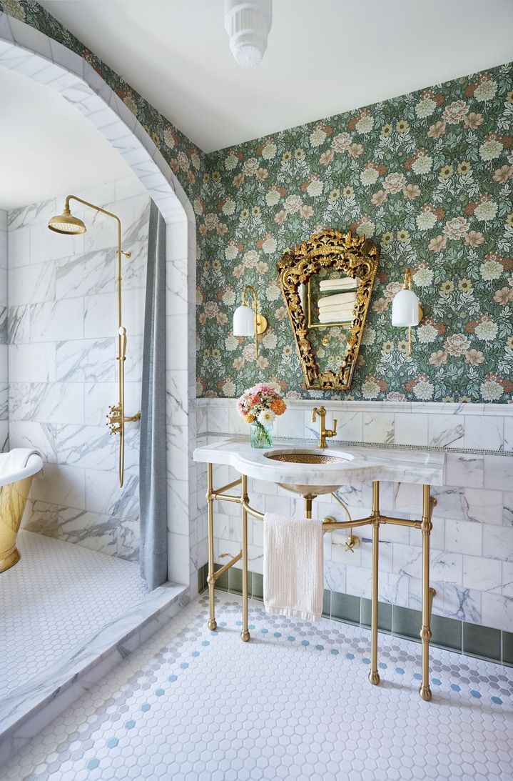 Luxurious bathroom with marble, floral wallpaper, gold fixtures, and ornate mirror.