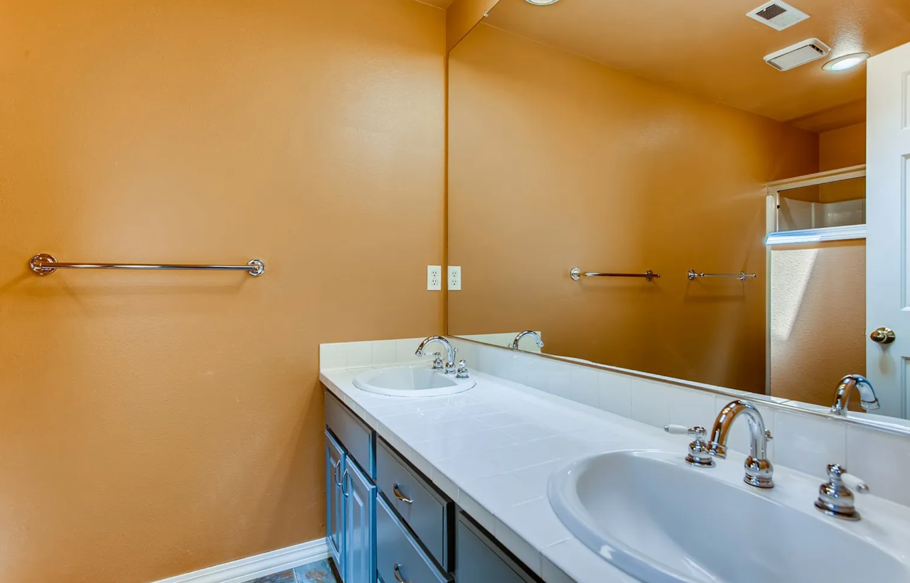 Bathroom with white countertops, two sinks, brown walls, and a large mirror.