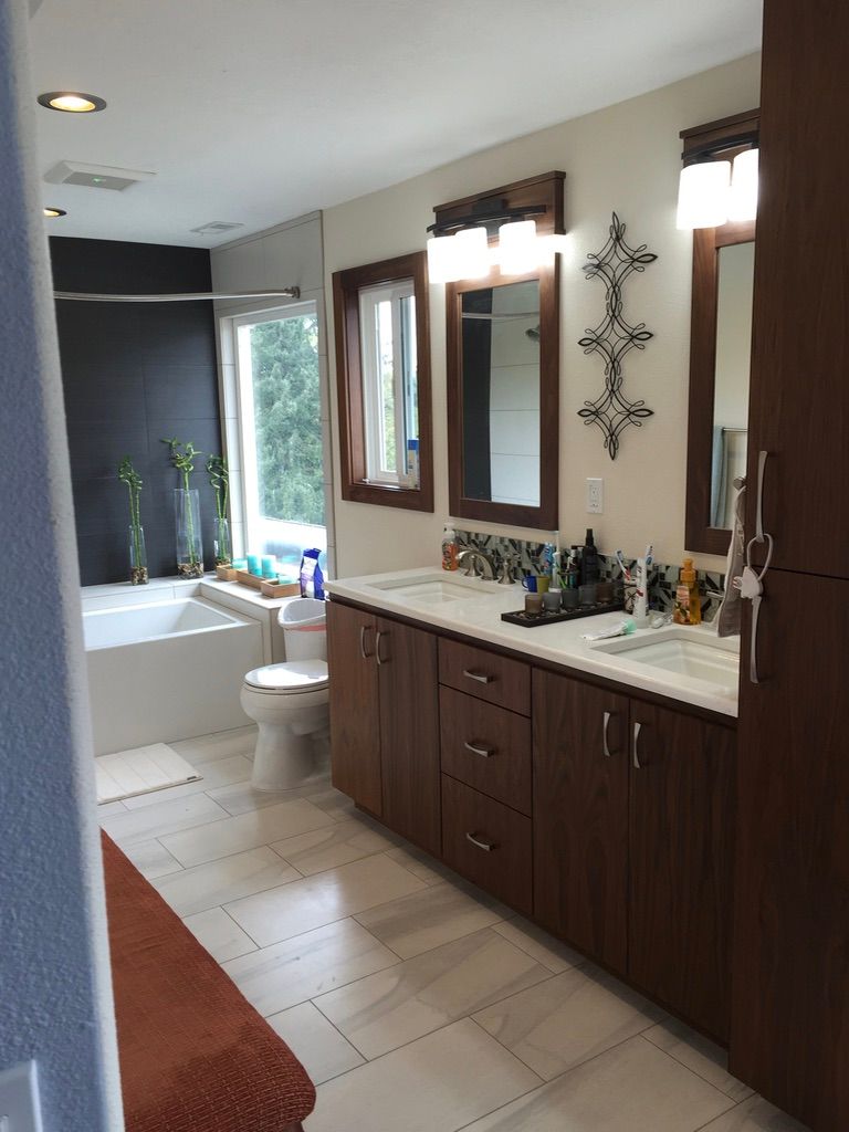 Bathroom with a tub, vanity with two sinks, and a window. Dark brown cabinets and white tile.