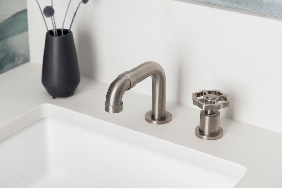 Brushed nickel faucet with star-shaped handle on a white countertop next to a black vase.