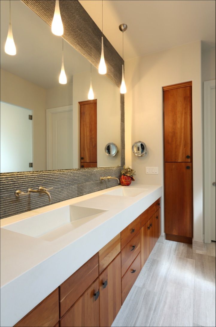 Modern bathroom with long white counter, wood cabinets, and teardrop pendant lights.