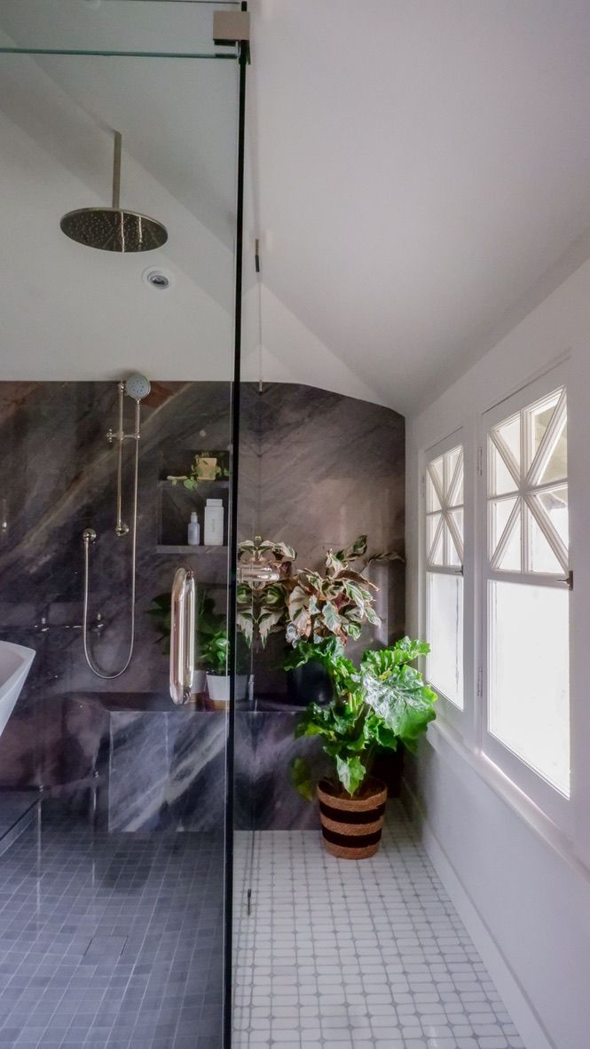Bathroom with glass shower, marble wall, plants, and small window.