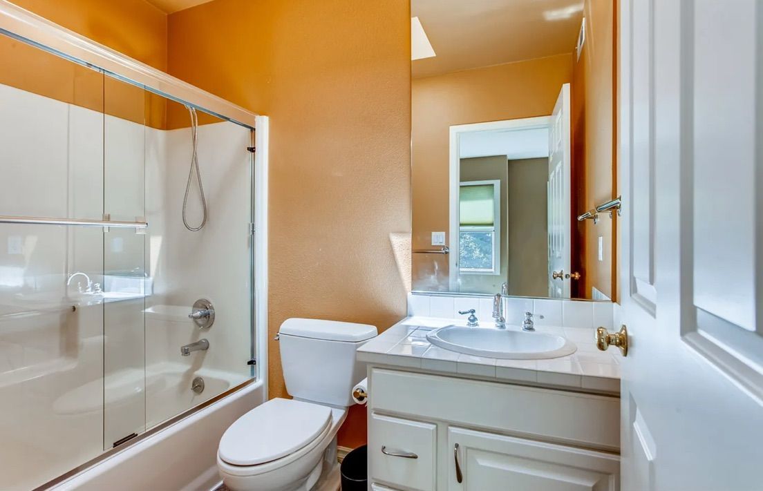 Bathroom with white toilet, sink, and shower. Orange walls and white trim.