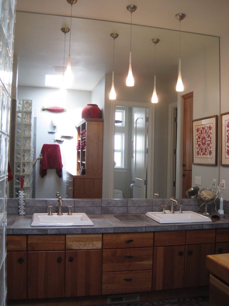 Bathroom with double sinks, large mirror, pendant lights, wood cabinets, and red accents.