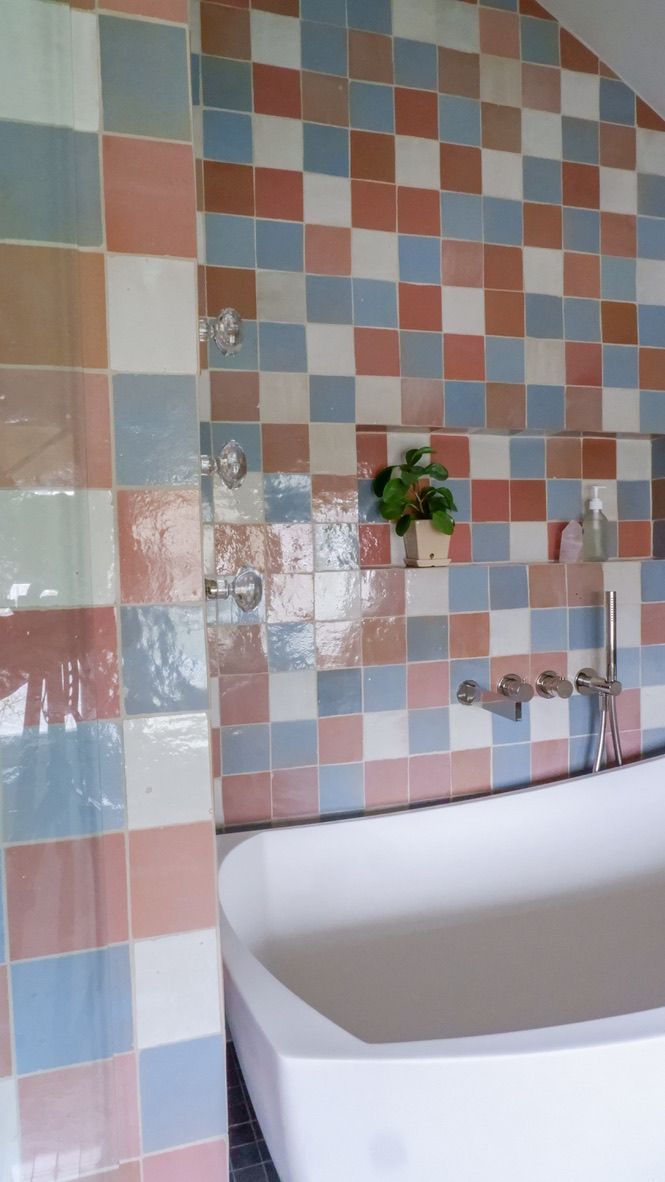 Bathroom with colorful square tiles in pink, blue, and white, around a white tub and a shower.
