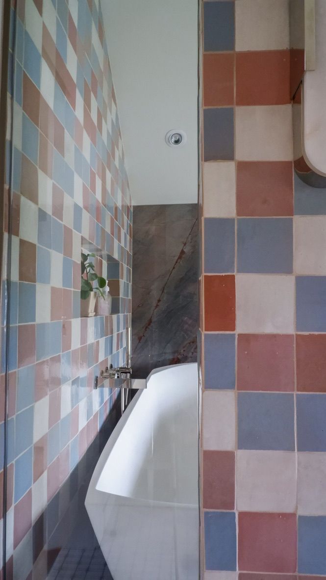 Bathroom with multi-colored square tiles on walls, a white bathtub, and a small plant in a niche.