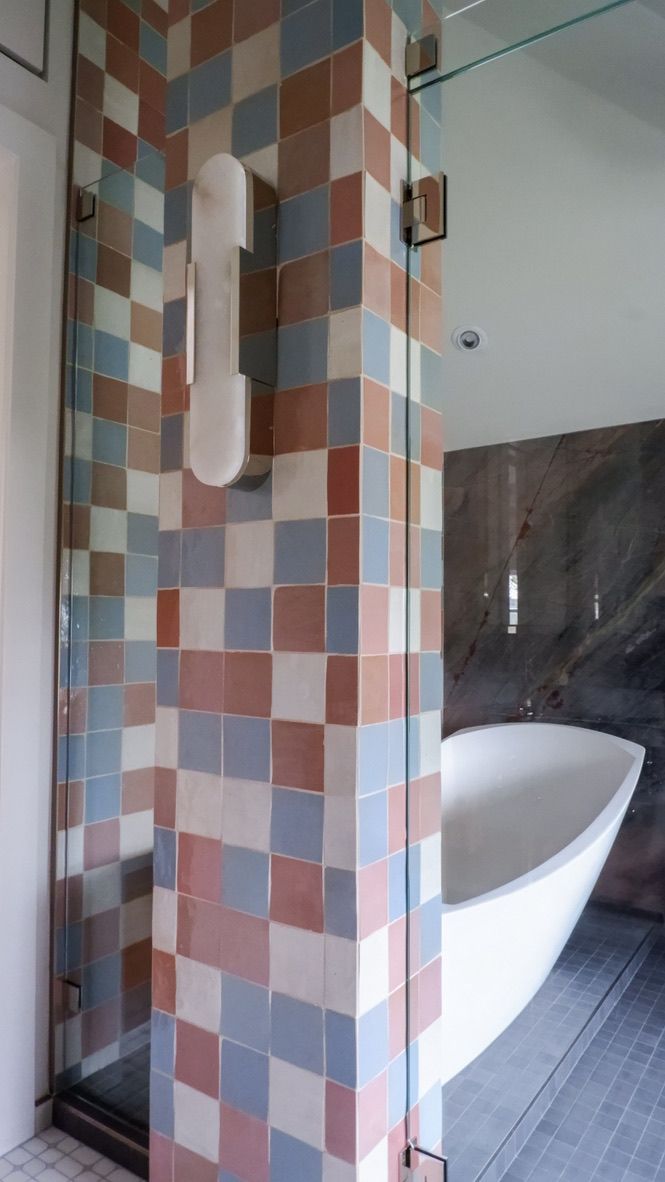 Shower column with multi-colored square tiles, clear glass door. White bathtub partially visible.