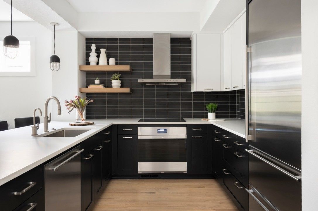 Modern black and white kitchen with stainless steel appliances, dark backsplash, and light wood floors.