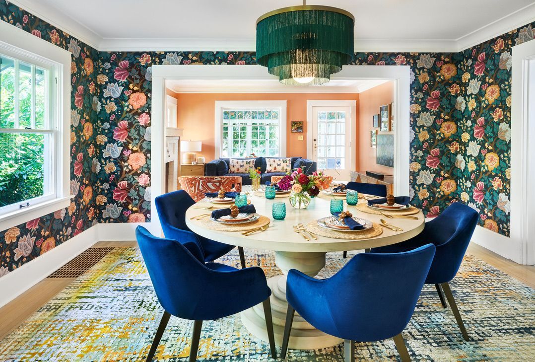 Dining room with floral wallpaper, round table, blue chairs, and a teal chandelier.