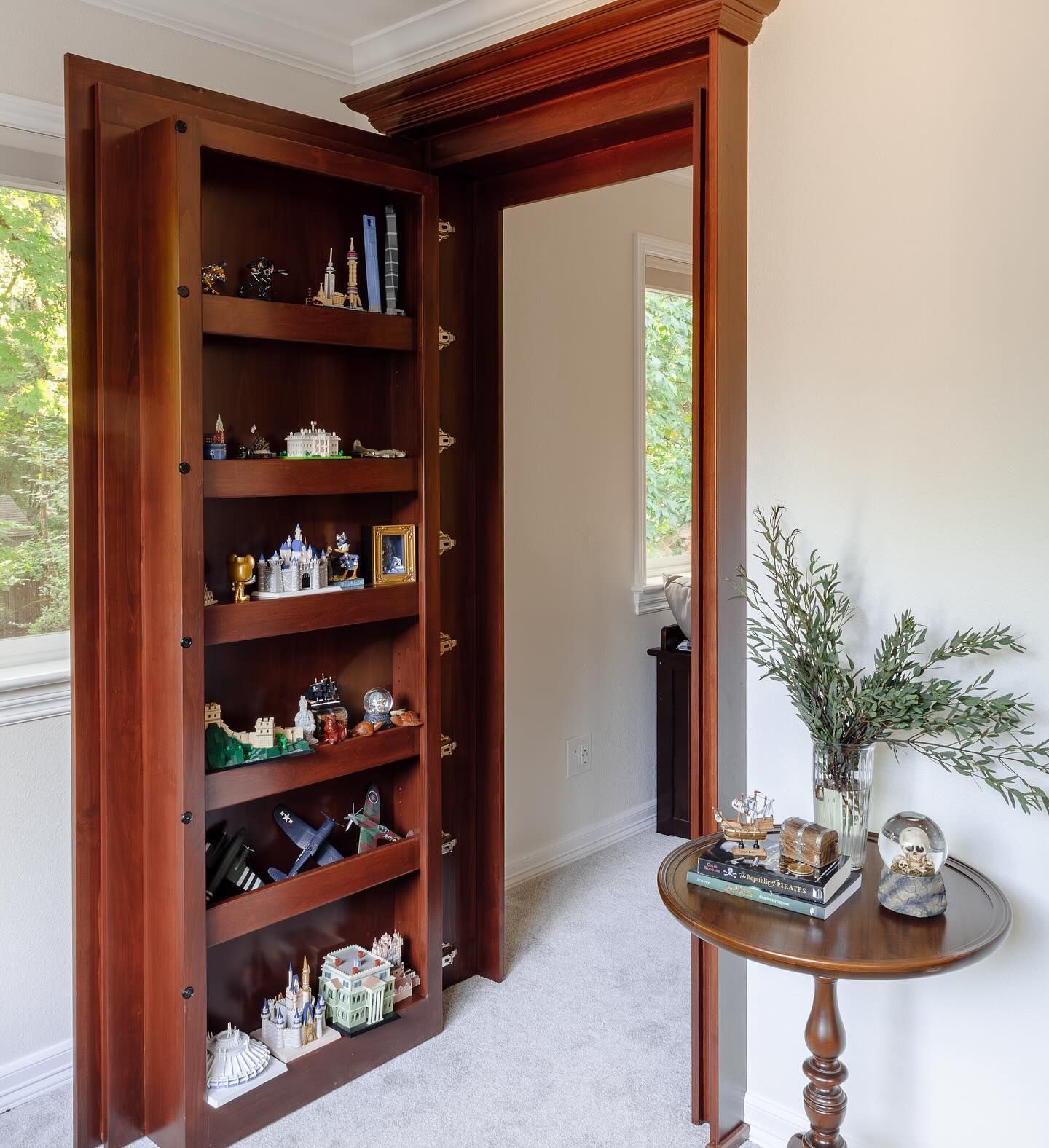 Wooden bookcase door leading to a room, with books and trinkets displayed on shelves.
