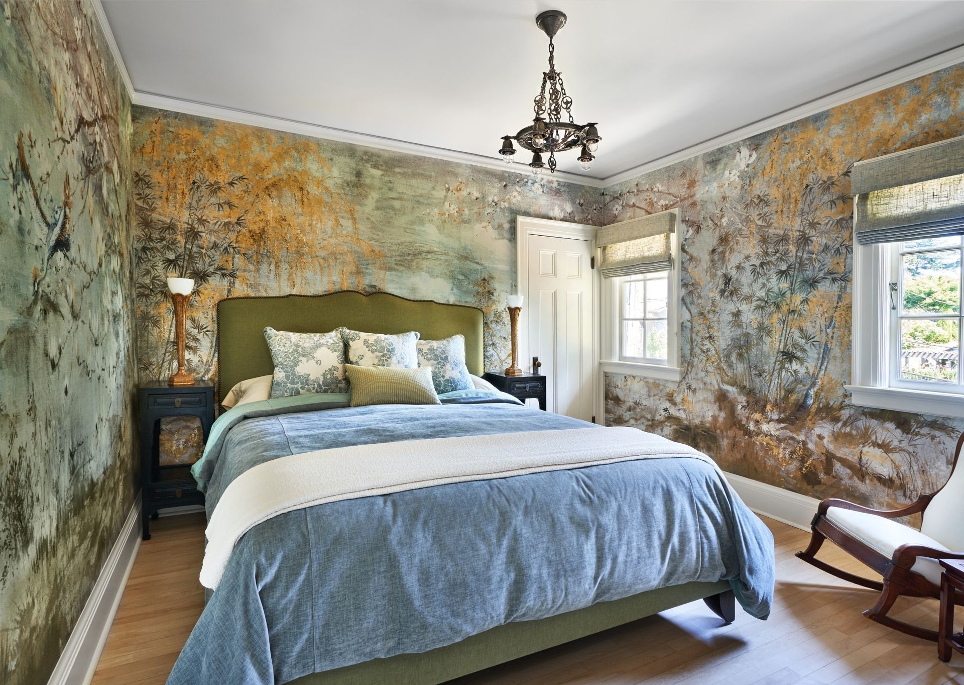 Bedroom with distressed wallpaper, blue bedding, green headboard, and small chandelier.