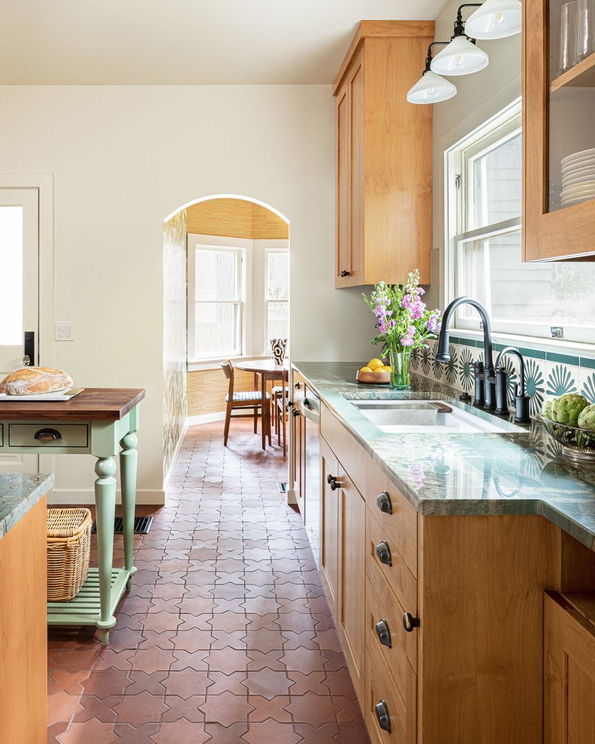Kitchen with light wood cabinets, brick floor, and archway to a breakfast nook.