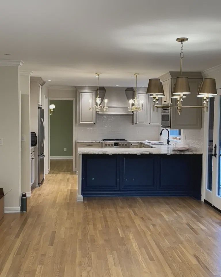 Kitchen with blue island, gray cabinets, wood floors, and gold light fixtures.