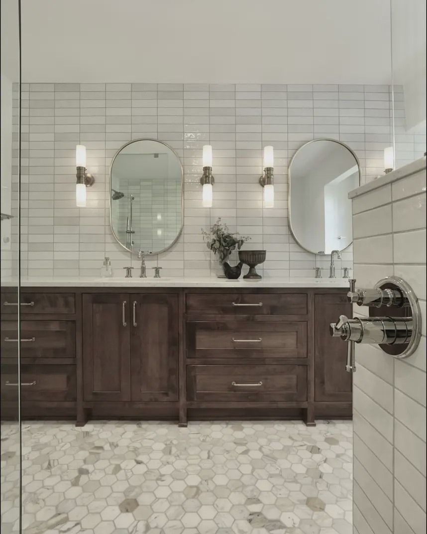 Bathroom with double vanity, oval mirrors, and honeycomb tile flooring. Dark wood cabinets.