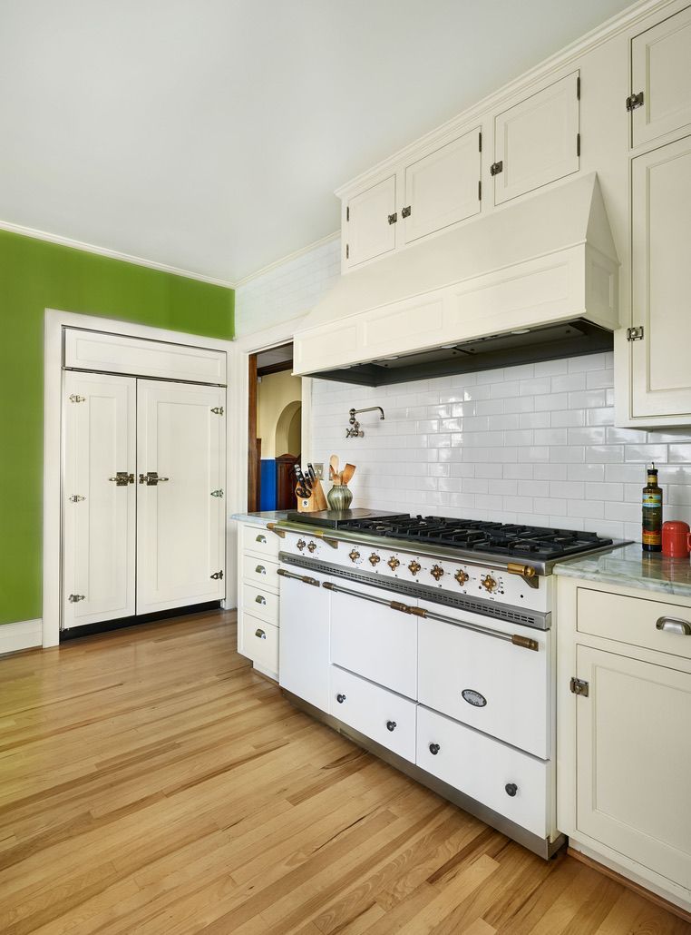 White kitchen with green accent wall, large stove, and wood flooring.