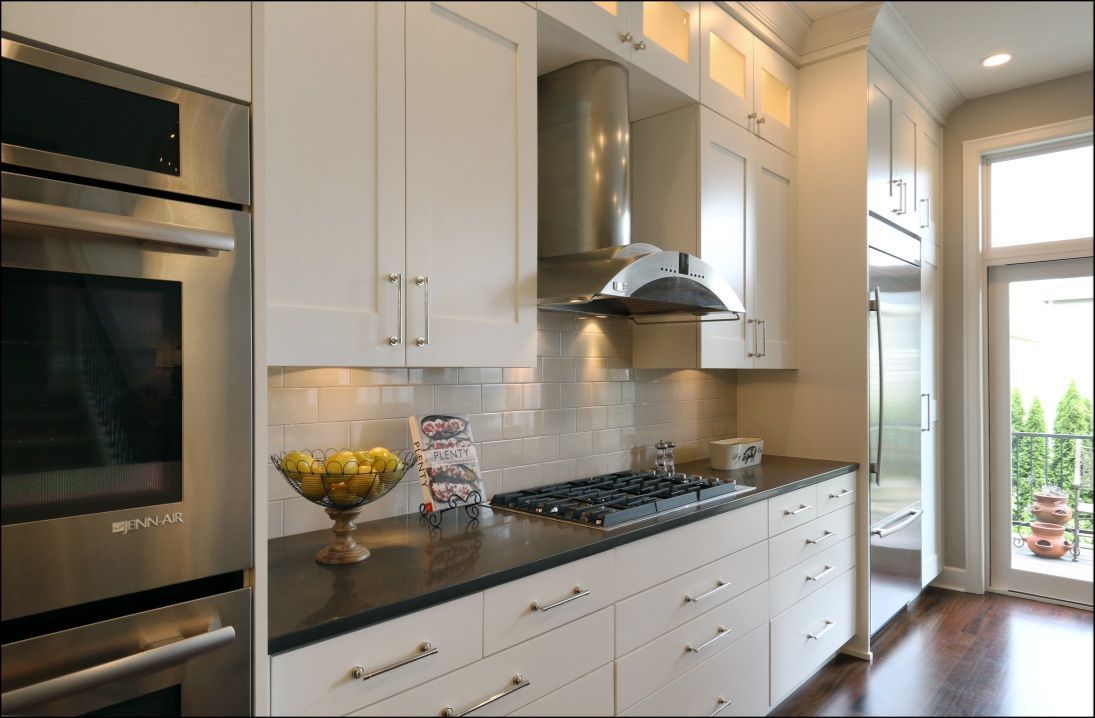 Modern kitchen with white cabinets, stainless steel appliances, dark countertop, and a door to a balcony.