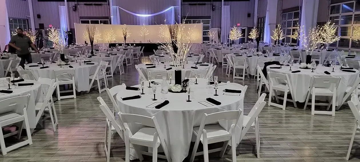 A spacious banquet hall set for an event with round tables featuring white tablecloths, black napkins, and lit centerpieces.