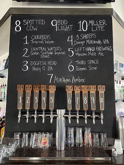 A chalkboard menu above ten beer taps displays numbered drink options, including Spotted Cow, Bud Light, and Miller Lite.