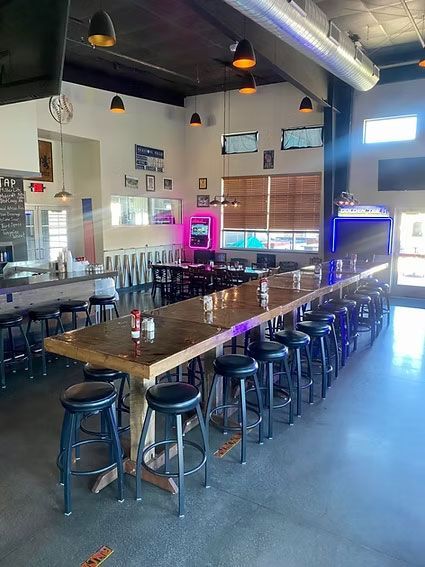 Interior of a bar with a long wooden bar, stools, tables, and ambient lighting.