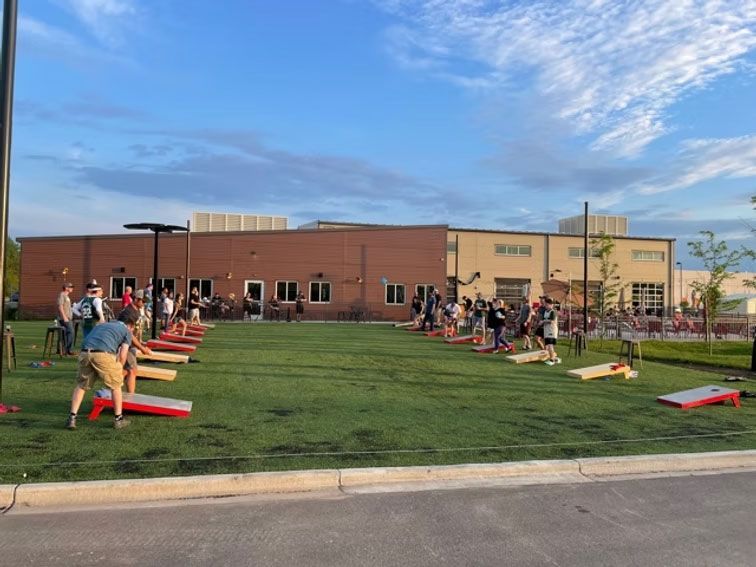 People playing cornhole on a green lawn in front of a brick building.