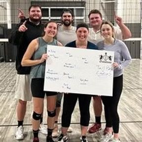 Group of people holding a whiteboard in an indoor court. Smiling, they are wearing sports attire.