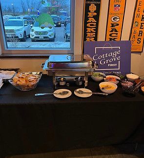 A buffet setup on a black tablecloth, featuring a silver chafing dish, a bowl of chips, and small bowls of toppings.