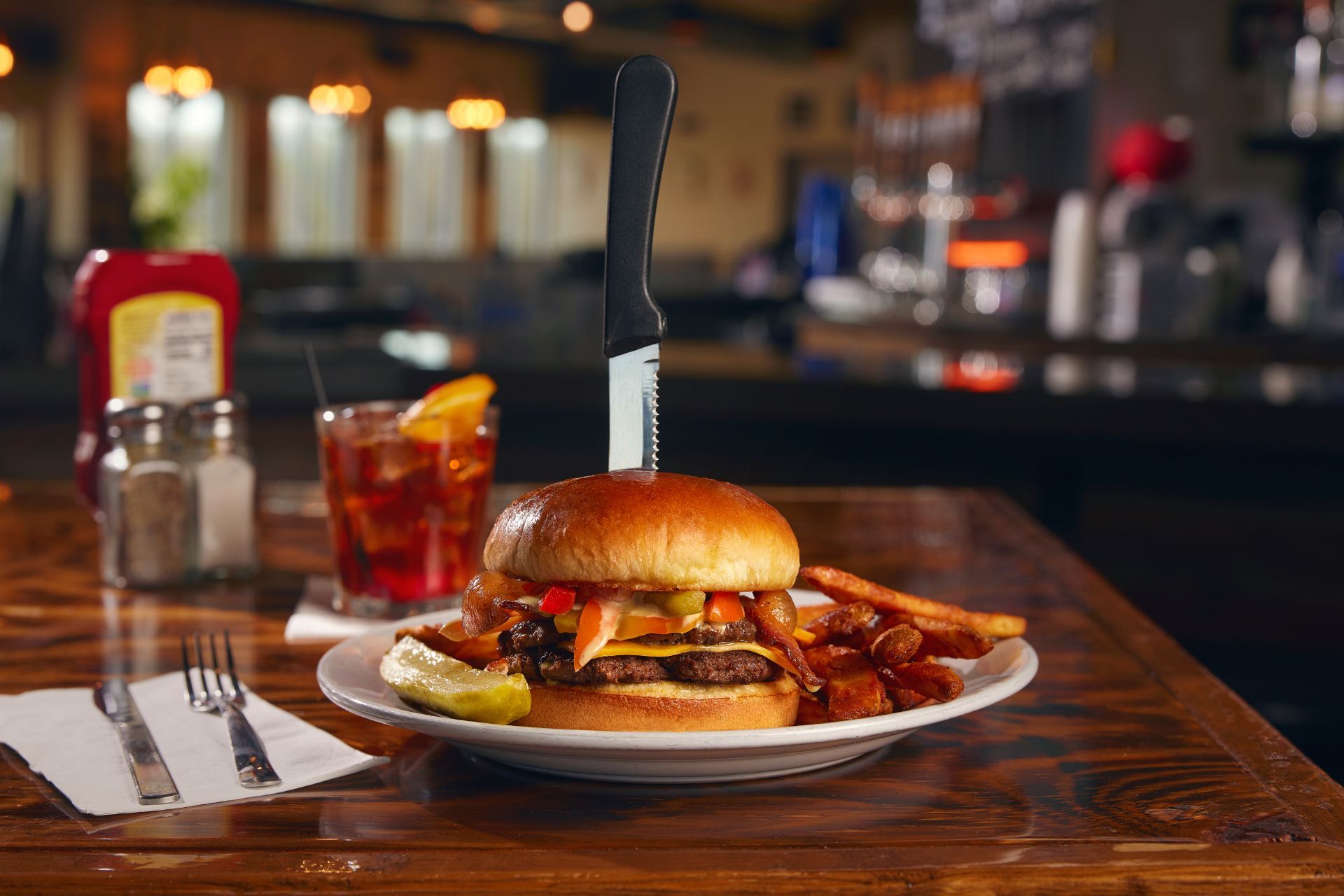 Burger with bacon and fries on a white plate in a dimly lit restaurant booth