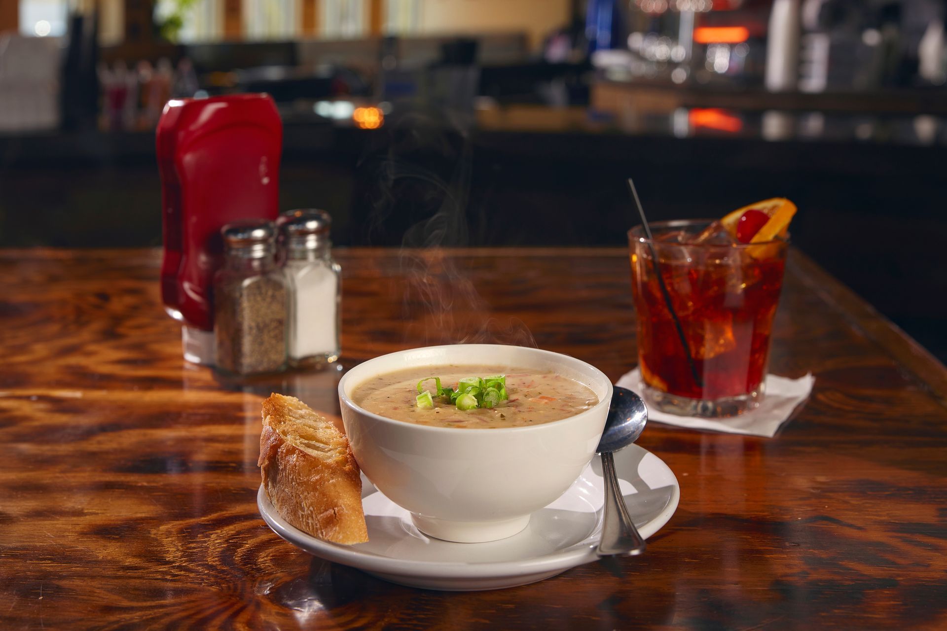 Bowl of soup with crackers on a restaurant table beside a glass of iced tea and condiments