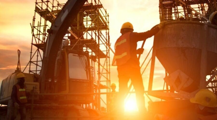 Construction workers pouring concrete at sunset.