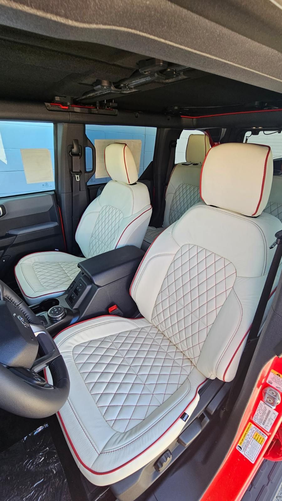Car interior with quilted white seat covers and red trim, viewed from the front passenger side