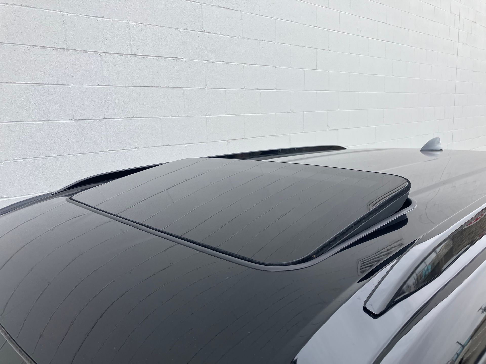 Dark car roof with a tinted sunroof and antenna against a light wall