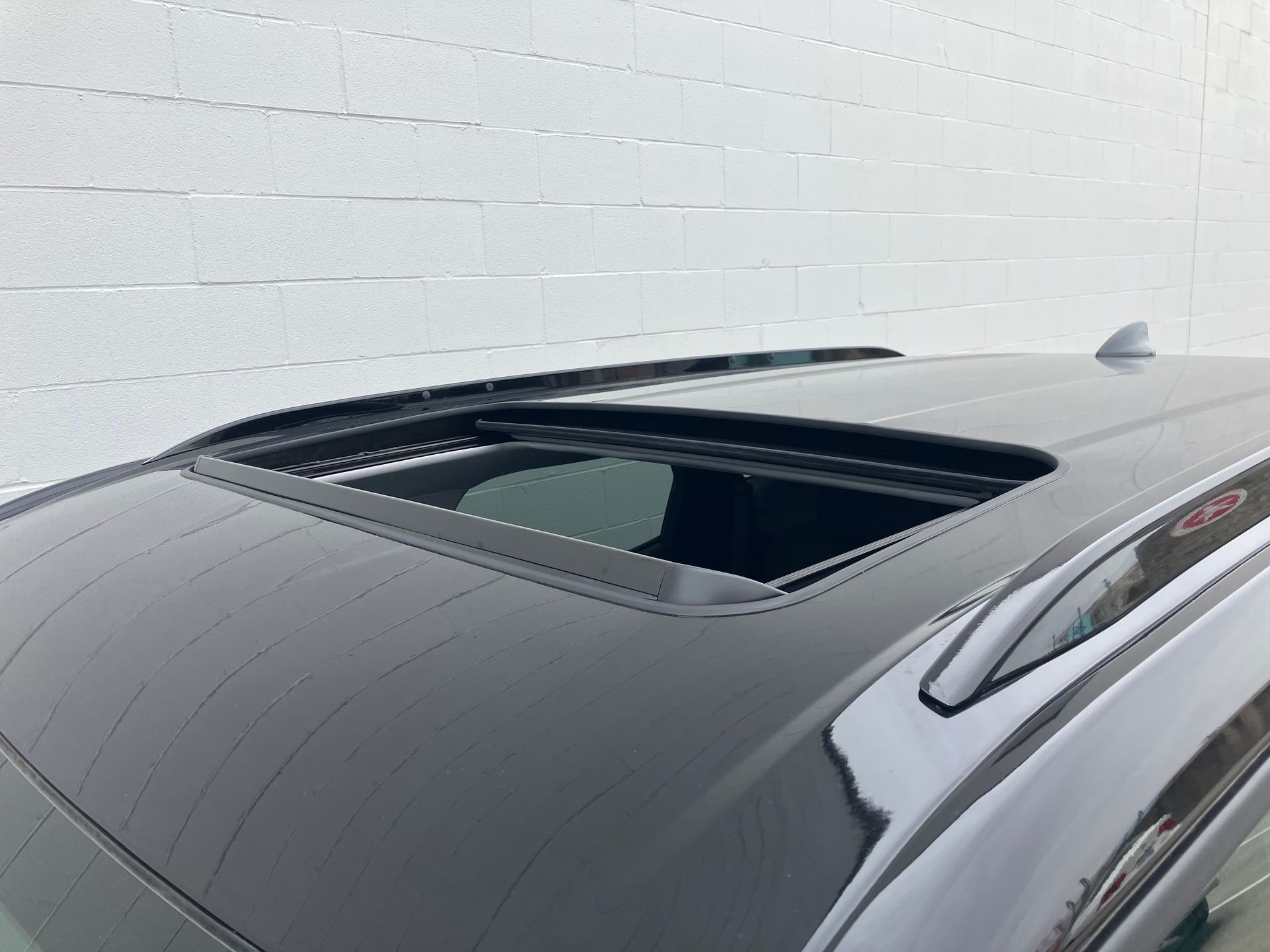 Black car roof with an open sunroof against a white wall