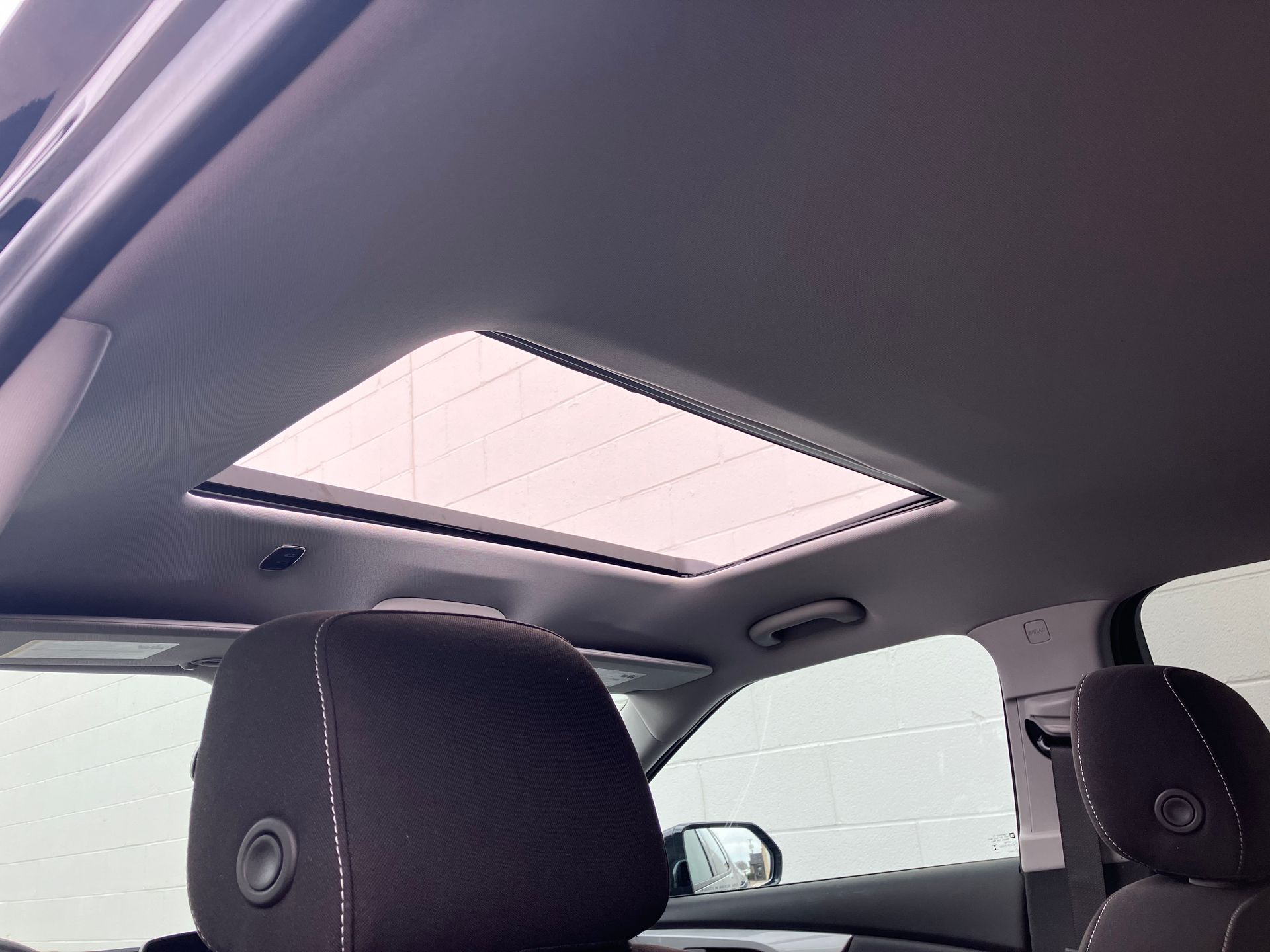 Car interior with black seats and an open sunroof showing the sky above.