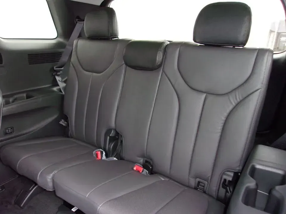 Rear car seat upholstered in black leather with three headrests and seat belts