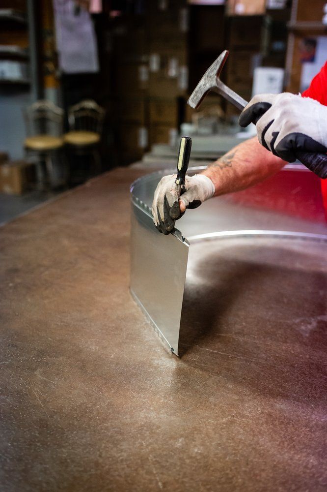 Person in gloves using a hammer and tool to bend metal on a work table.