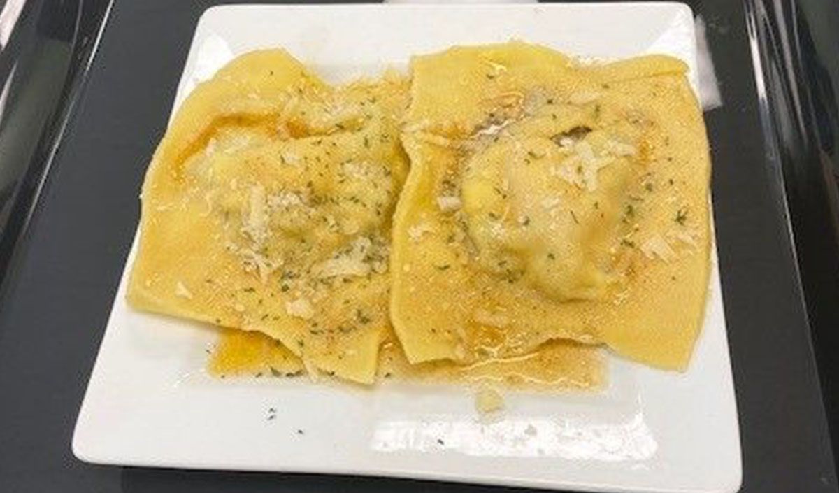 A white plate topped with two ravioli on a black tray.