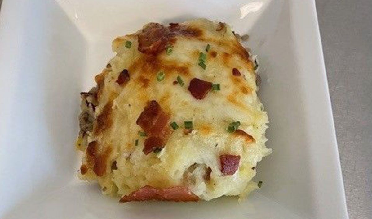 A white plate topped with mashed potatoes and bacon.