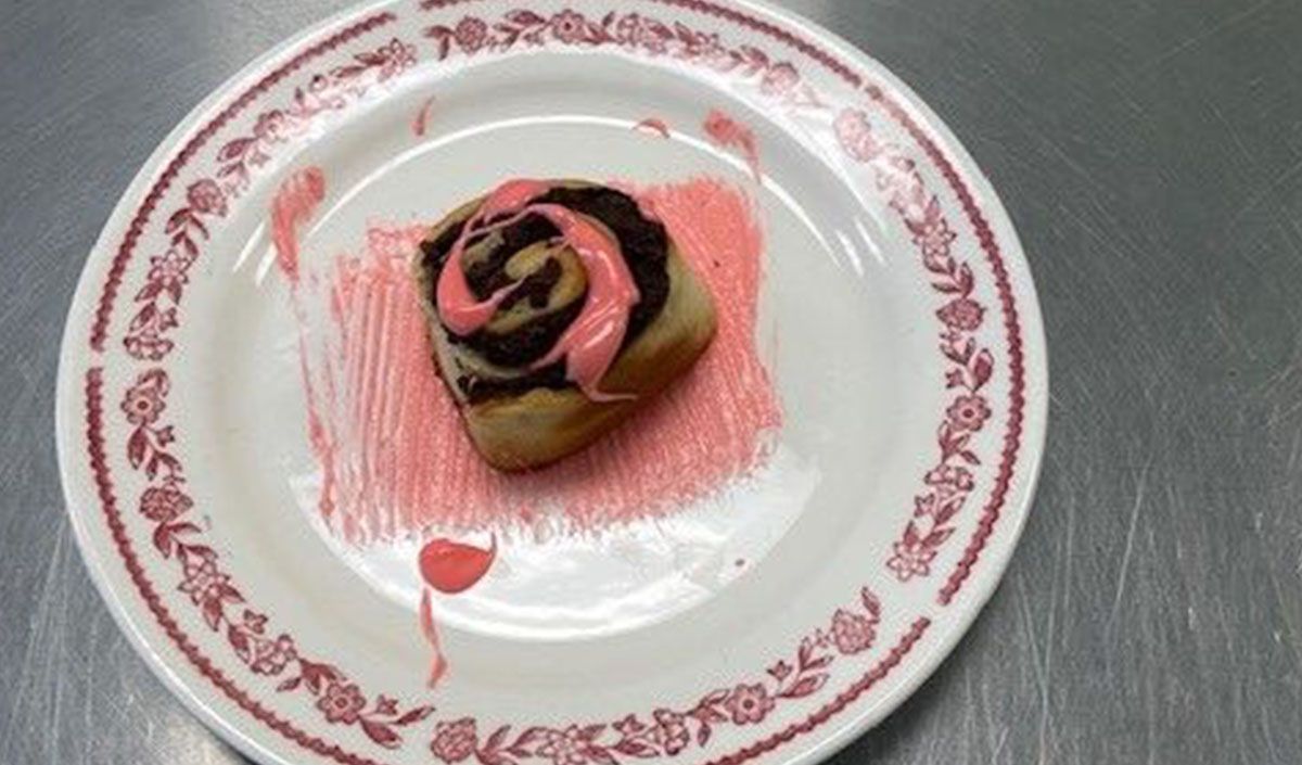 A white plate topped with a chocolate cinnamon roll with pink frosting.