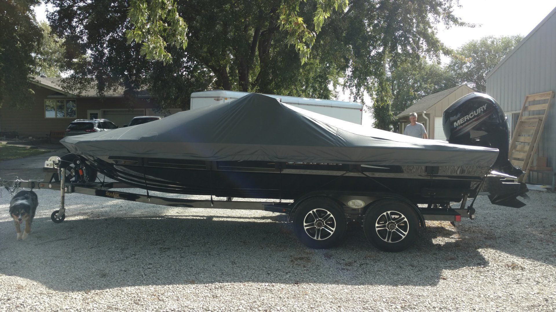 A boat with a cover on it is parked in a gravel lot.