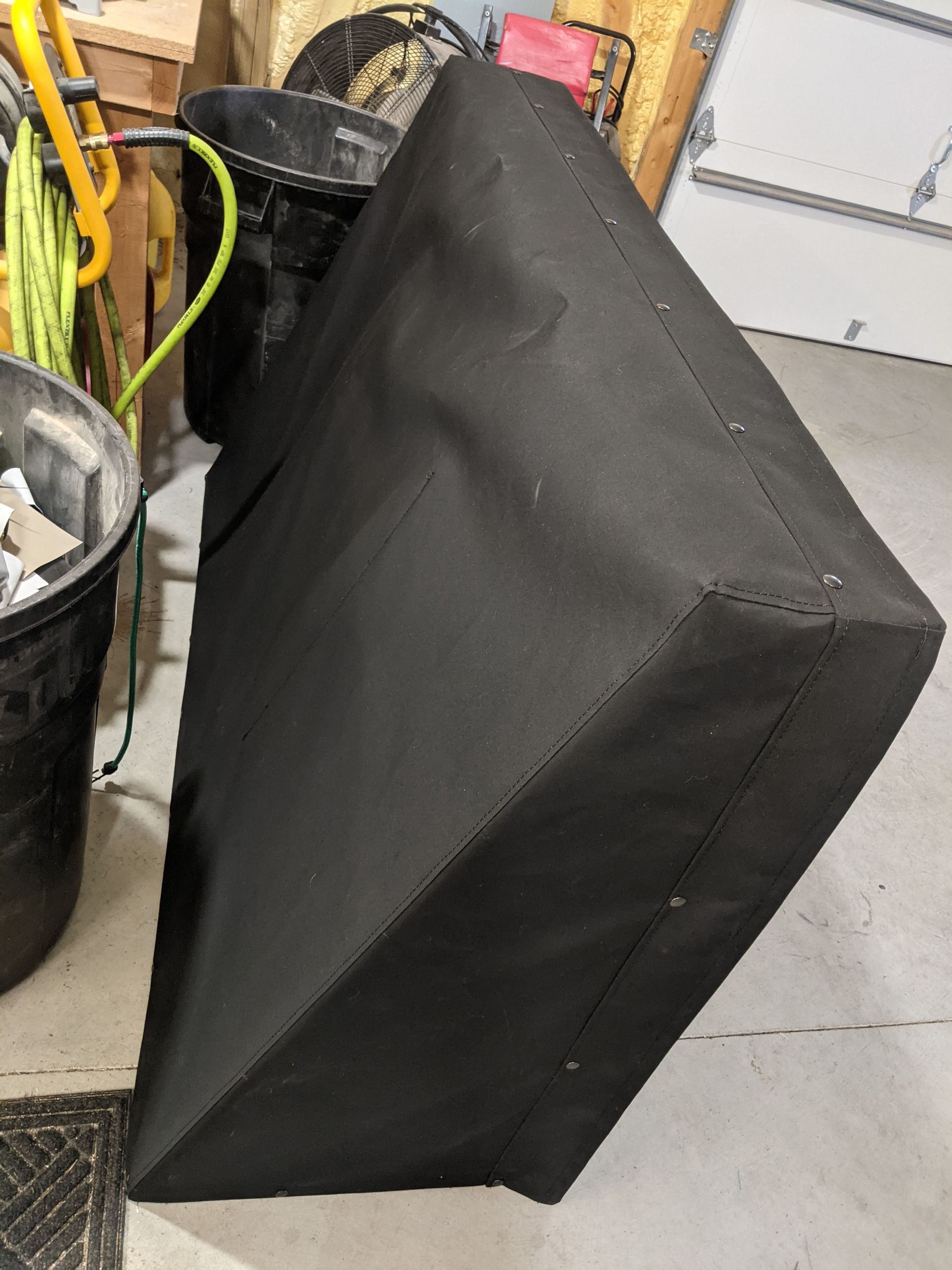 A black box is sitting on the floor in a garage next to a trash can.