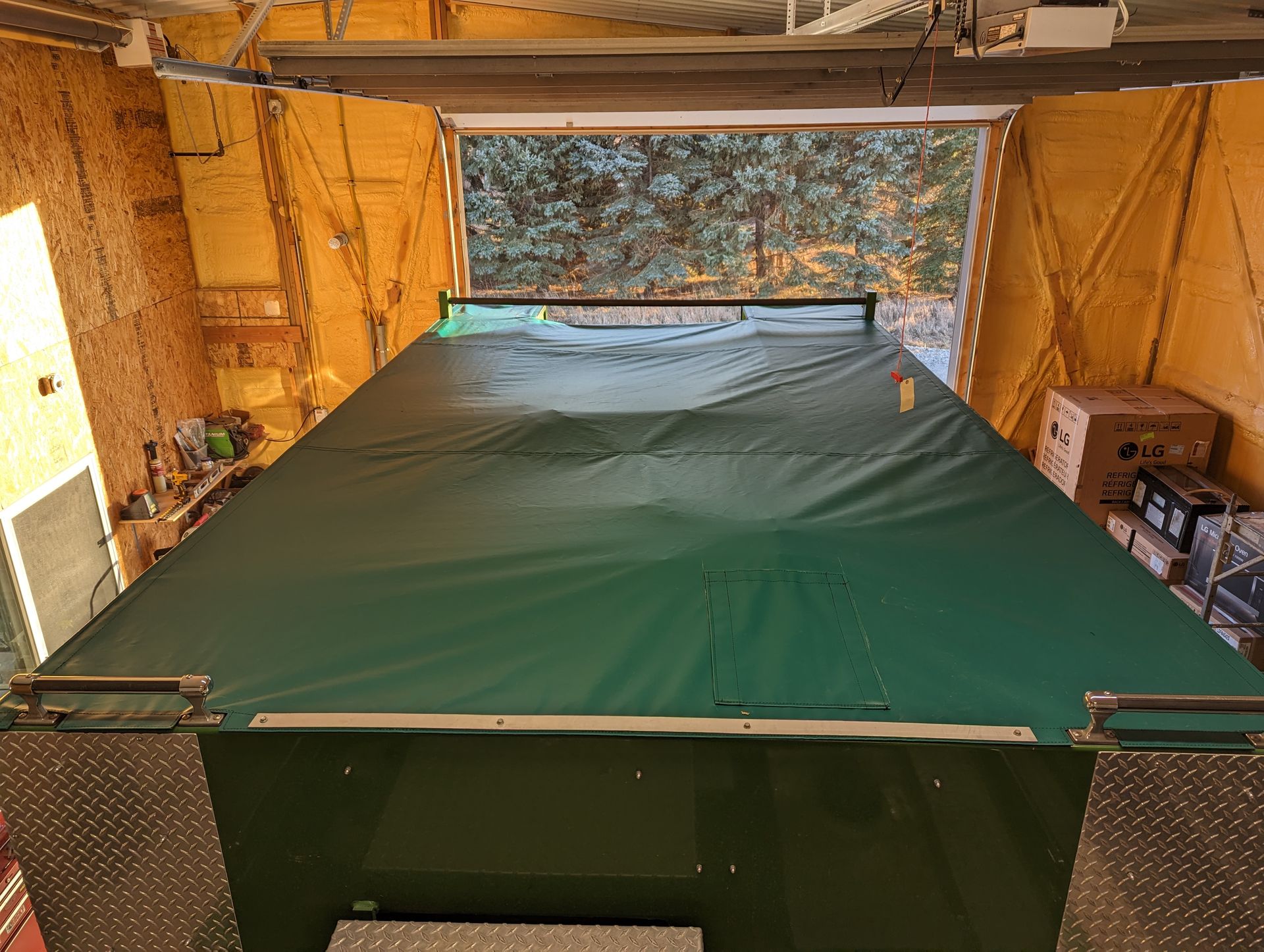 A green tarp is covering a pool table in a garage.