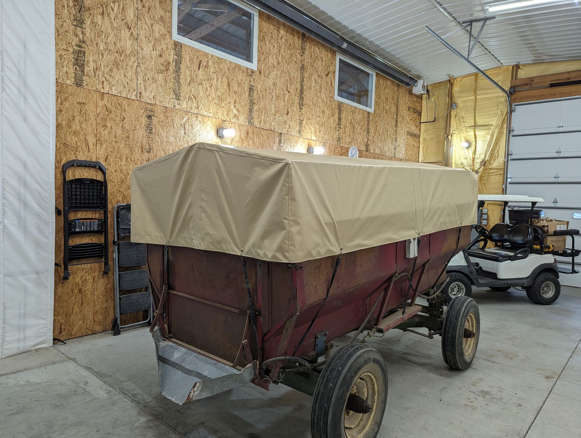 A wagon with a cover on it is parked in a garage next to a golf cart.