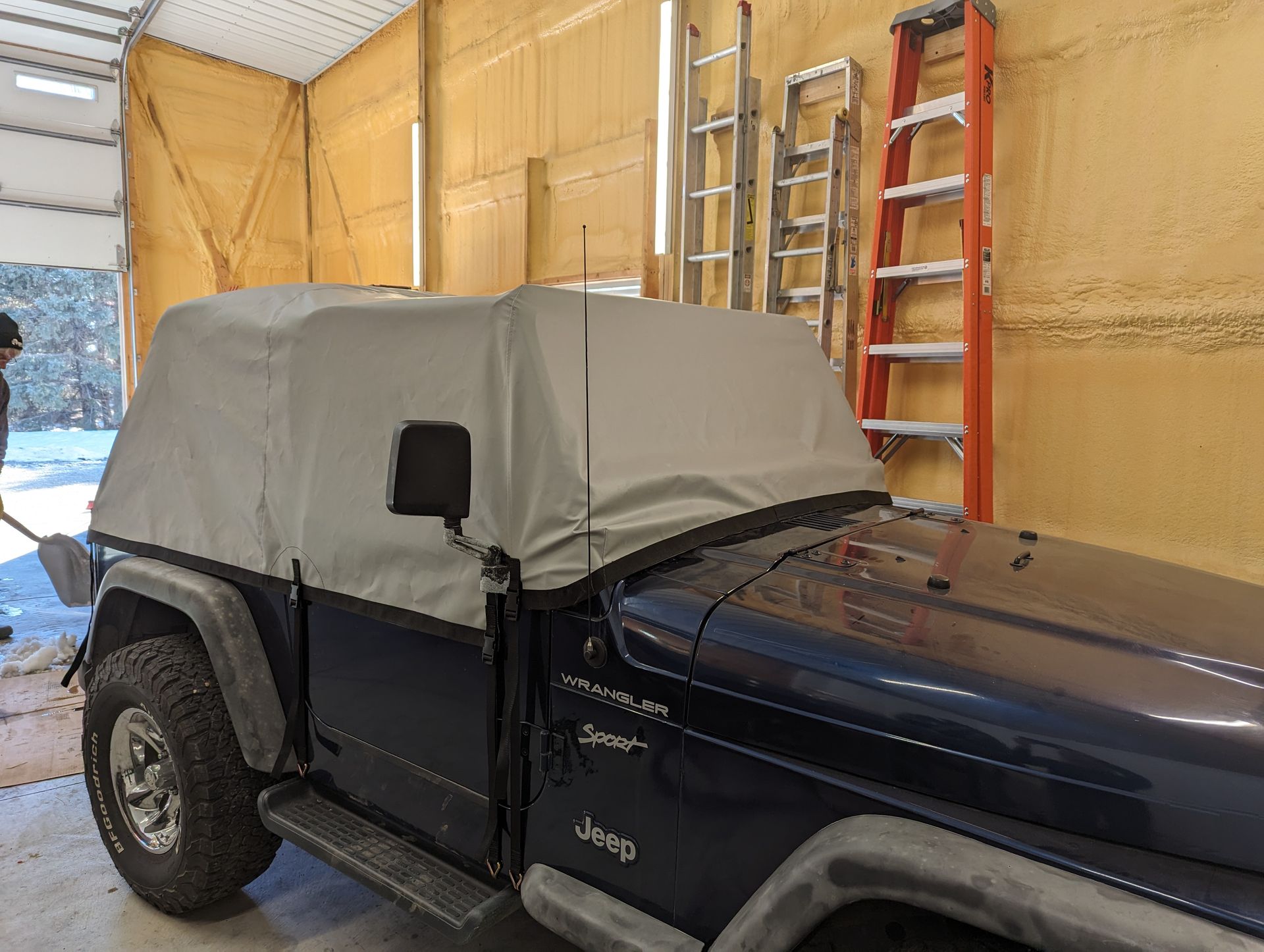 A blue jeep with a canopy on top of it is parked in a garage.