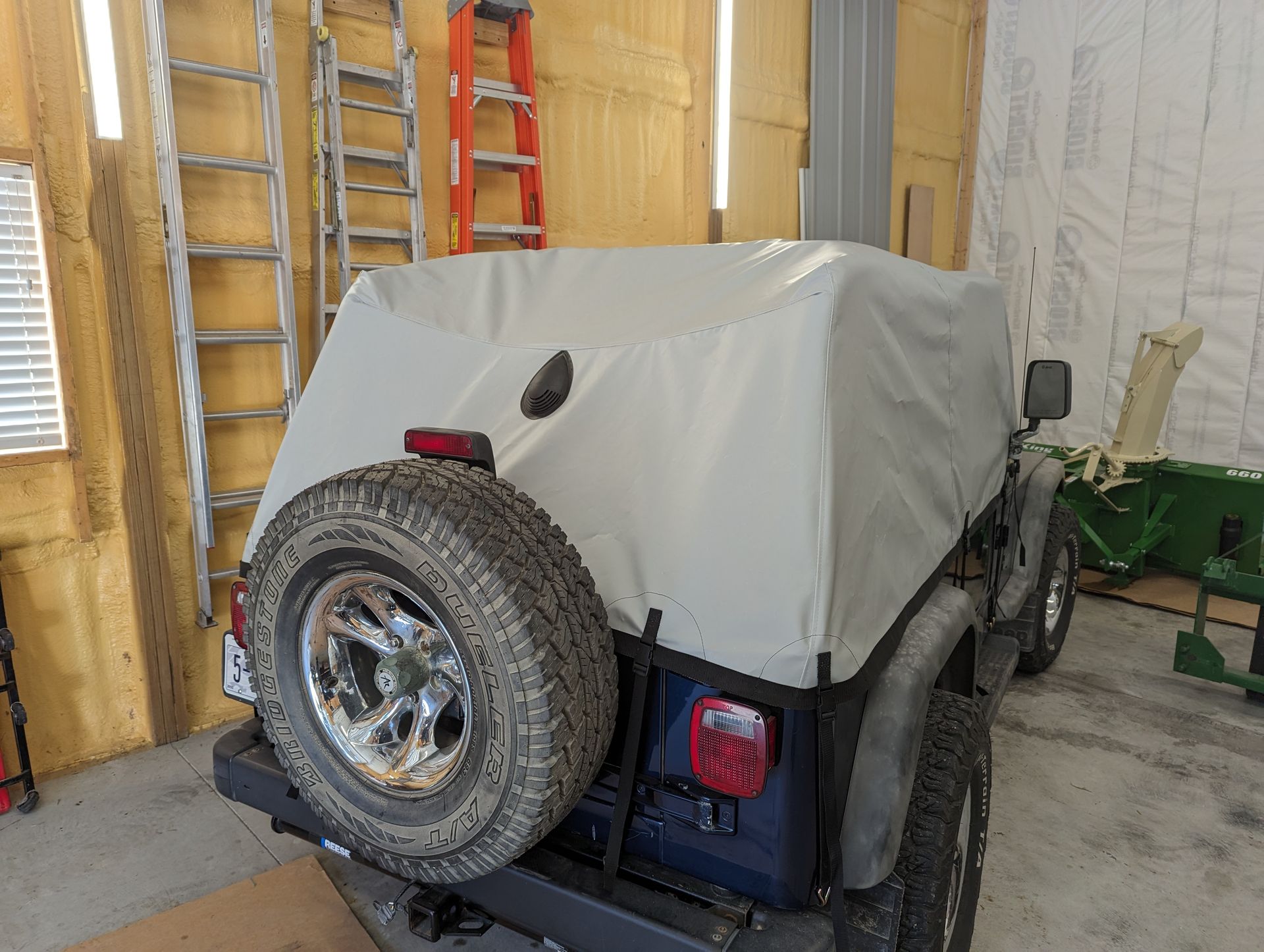 A jeep with a cover on it is parked in a garage.