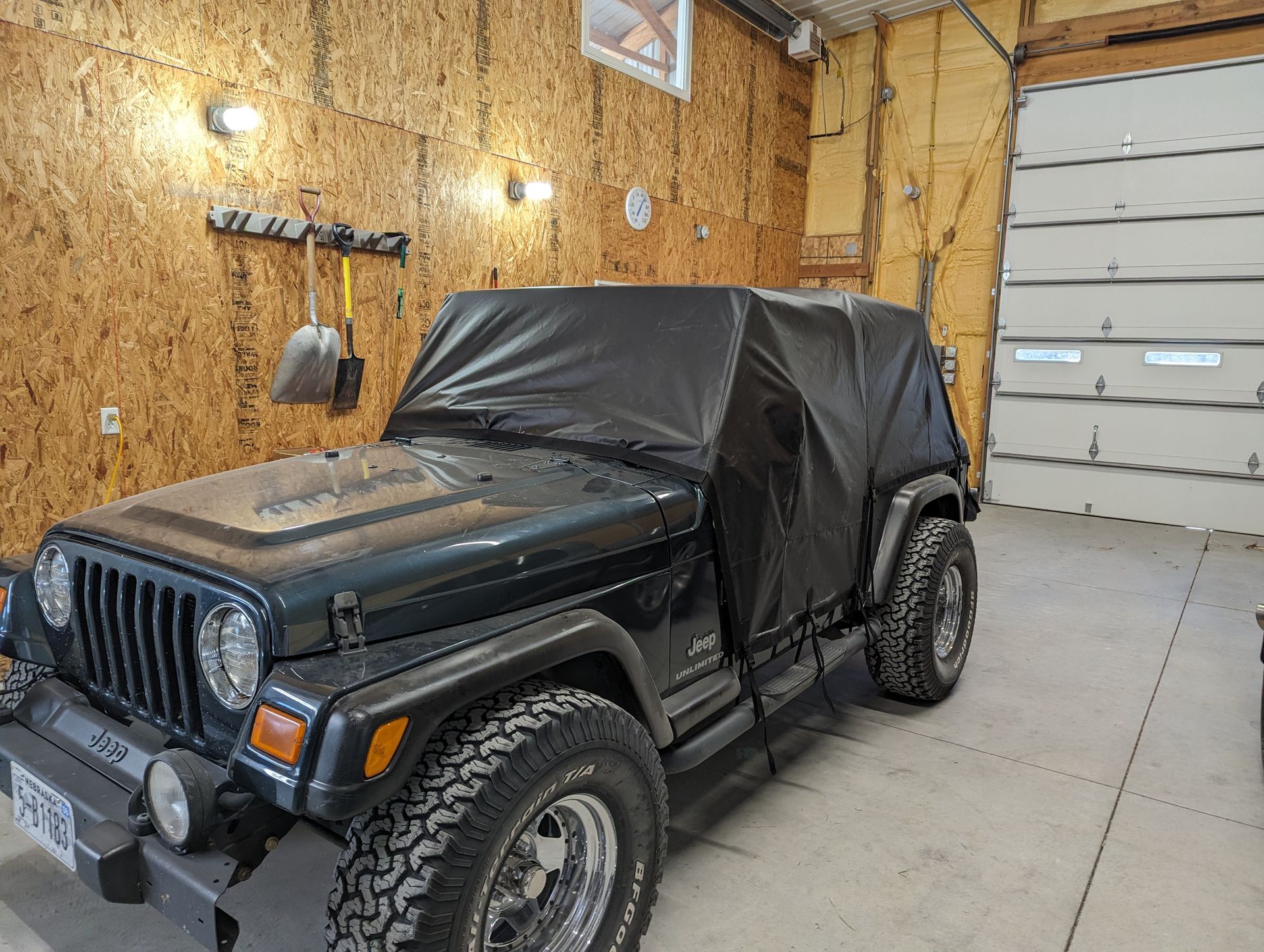 A black jeep is parked in a garage with a black cover on it.
