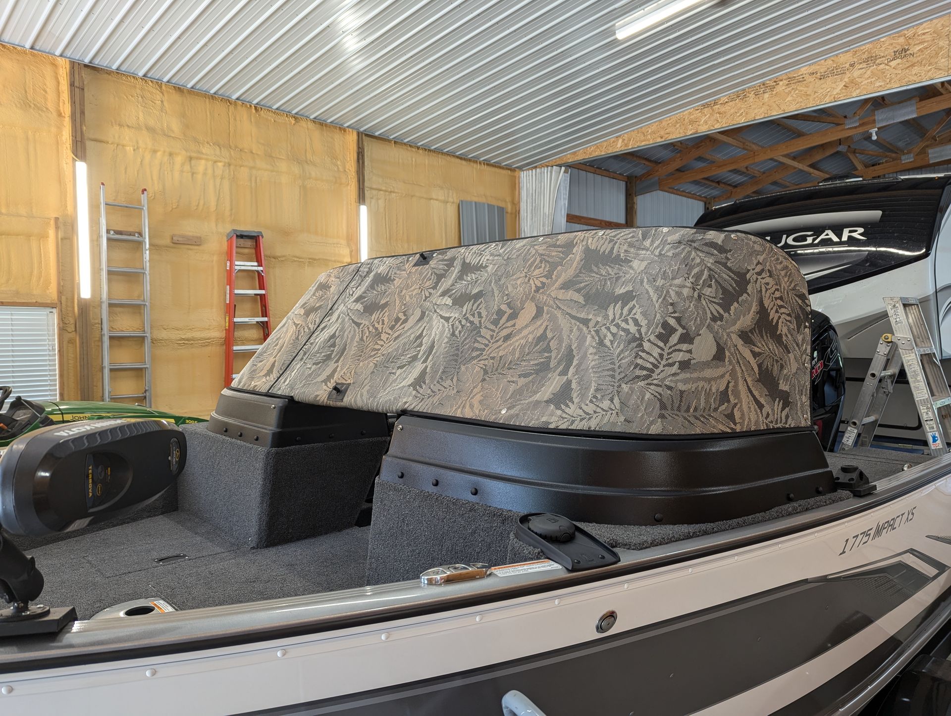 A boat is sitting in a garage with a camouflage cover on it.